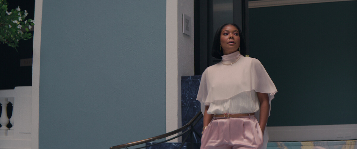 Gabrielle Union strolls into an office in a drapey pink capelet shirt and pink silk pants in a still from ‘The Perfect Find.’