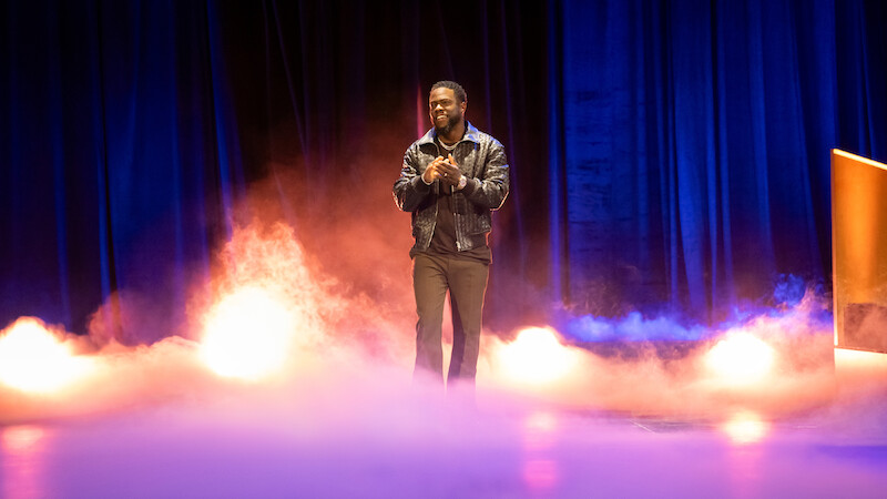 Kevin Hart stands on stage as fog surrounds him.