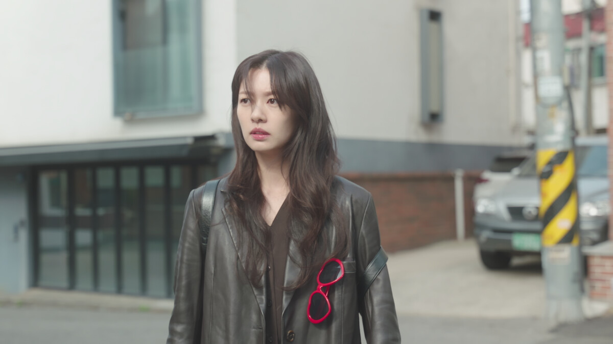 Jung So-min as Bae Seok-ryu stands in front of a building wearing a black leather jacket in ‘Love Next Door.’