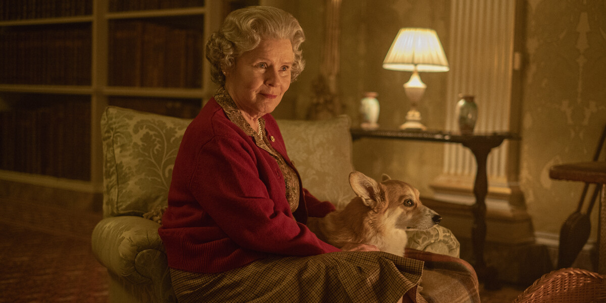 The queen sitting on a couch with a corgi dog