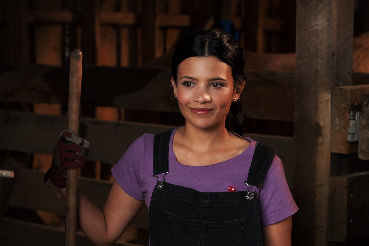 Nikki Rodriguez as Jackie wearing overalls in a barn in ‘My Life with the Walter Boys’ Season 2.