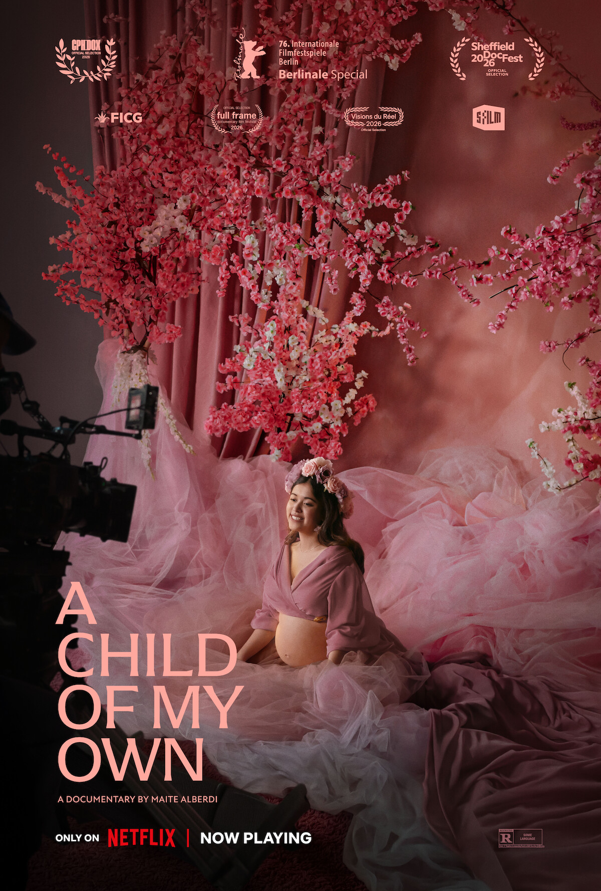 Pregnant woman in a pink dress and flower crown sits with hands on belly in a studio filled with pink tulle and cherry blossom branches, being filmed for a documentary titled "A Child of My Own," now playing on Netflix.