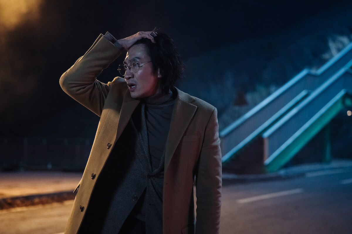 Lee Kwang-soo stands in an empty street in the dark with his hand clasping the top of his head in an image from the series ‘Karma.’