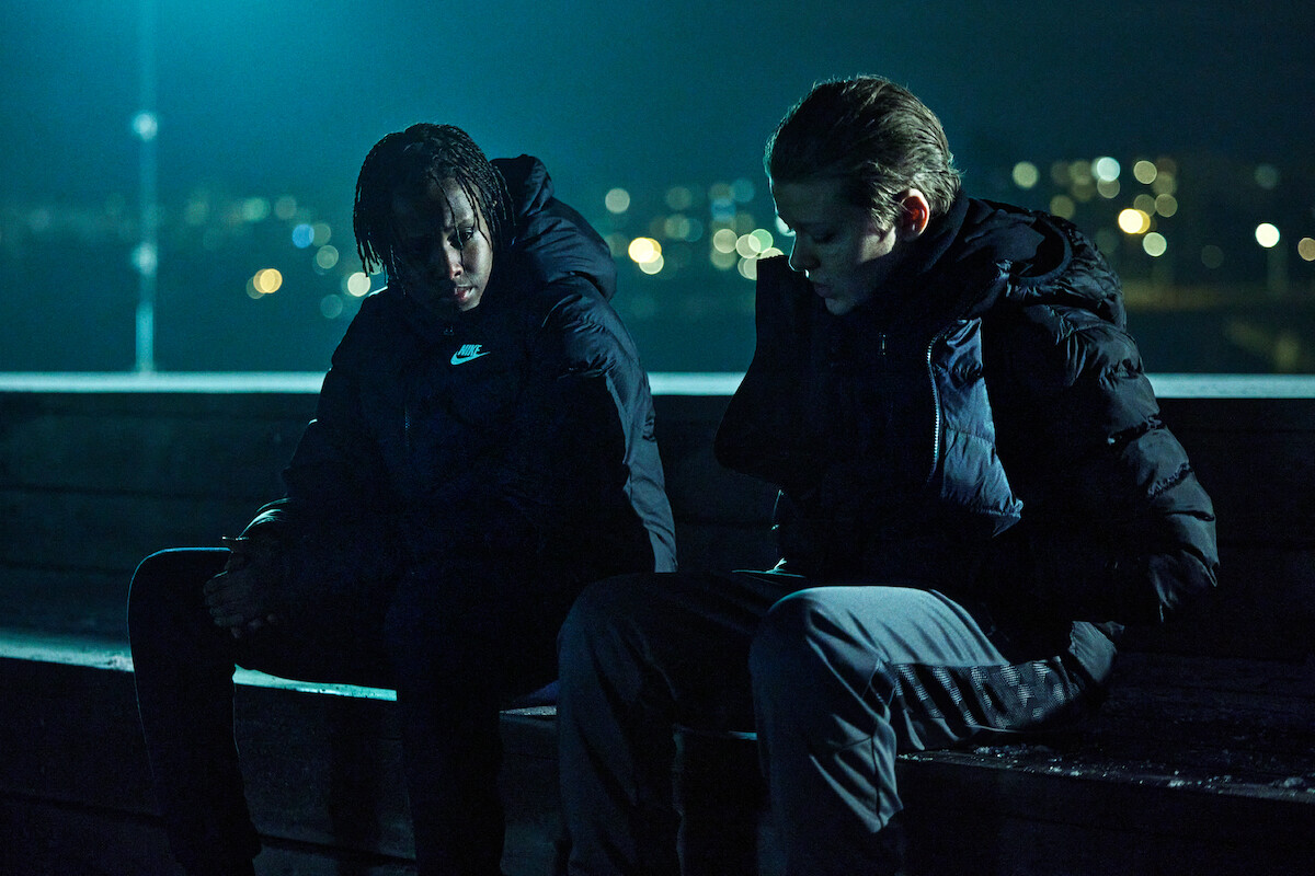 Yasir Hassan as Billy and Olle Strand as Dogge sit together outdoors at night in ‘Deliver Me’