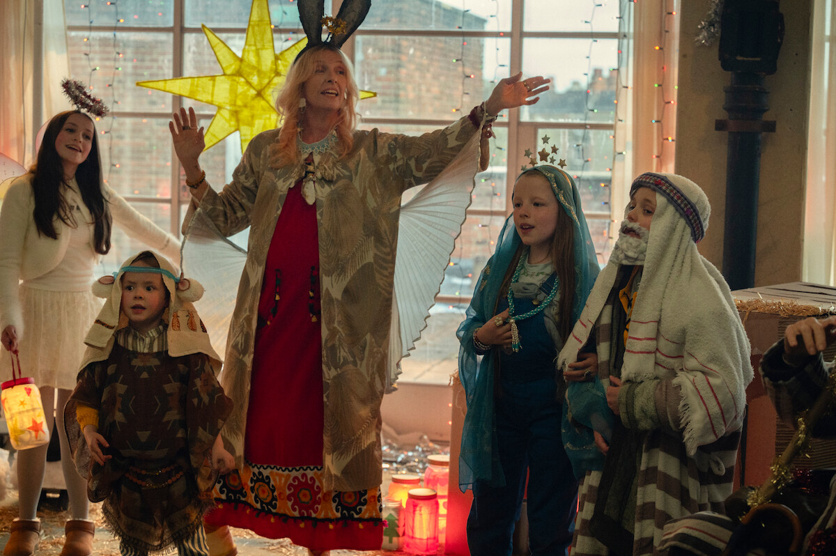 Children and adults in festive costumes perform in a brightly decorated room with a star lantern, creating a joyful and celebratory mood.