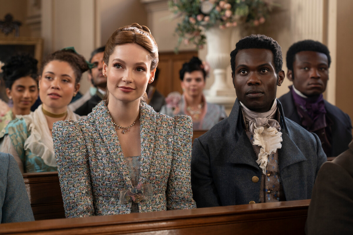 Victor Alli as John Stirling and Hannah Dodd as Francesca Bridgerton stand in a sitting room together smiling in Season 3 of ‘Bridgerton’