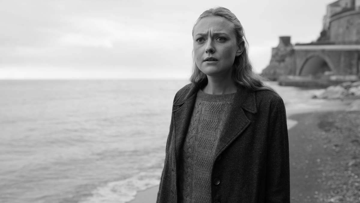 Black-and-white photo of Dakota Fanning and Marge standing on a beach with a concerned expression in ‘Ripley’