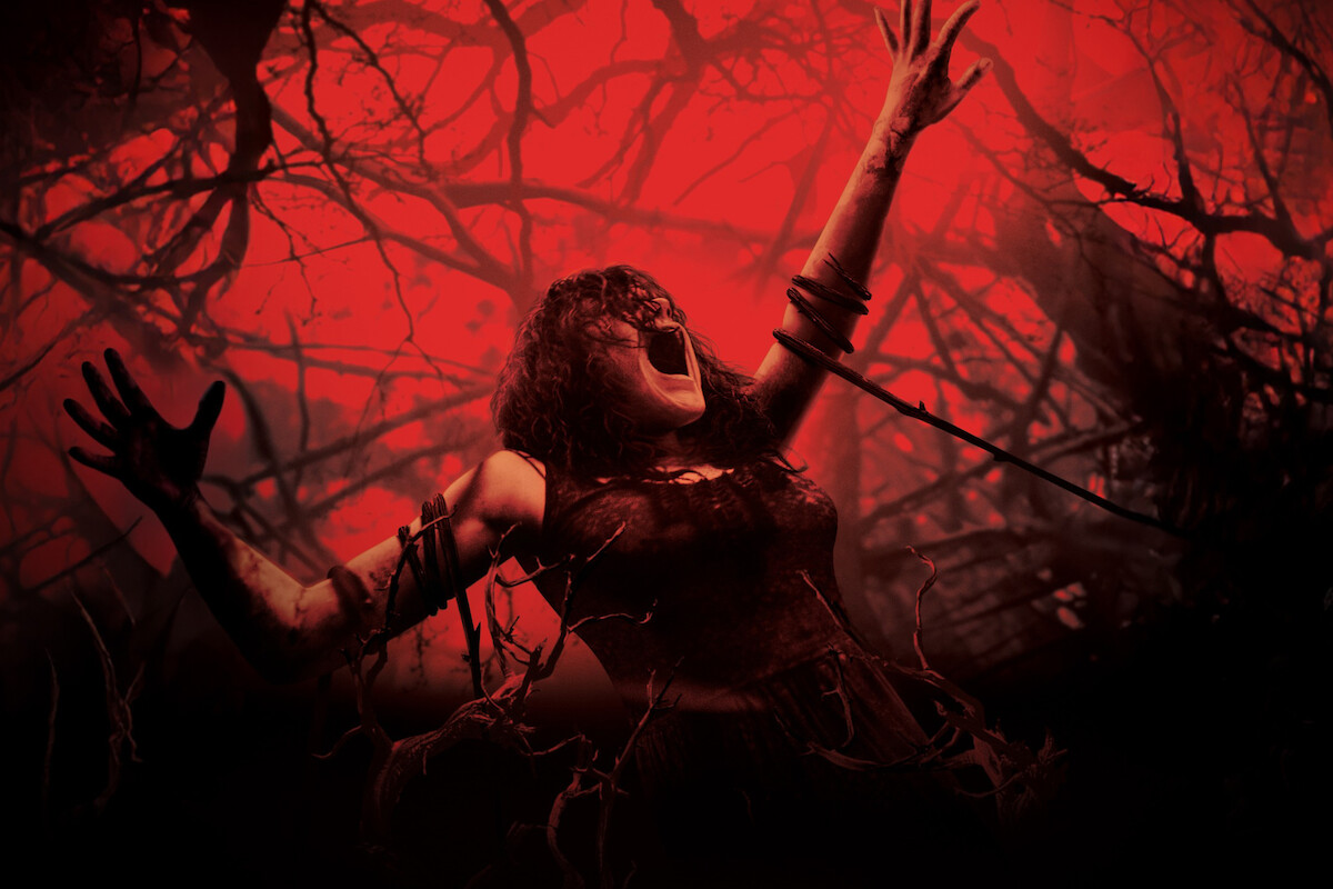 A woman screaming with arms raised, entangled in dark branches, in a haunted forest with a dramatic red and black background, evoking a scene of horror and supernatural tension.