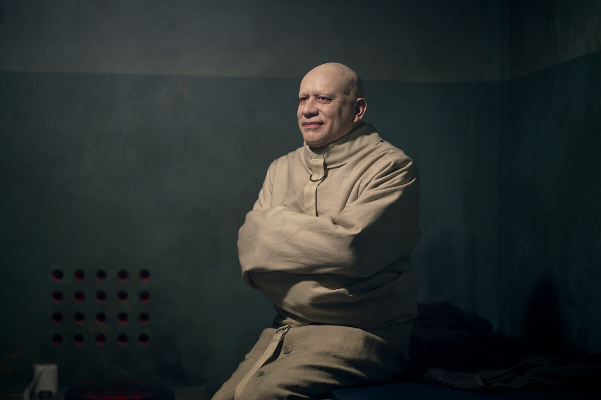 Fred Armisen as Uncle Fester sits in a straight jacket smiling in ‘Wednesday’ Season 2.