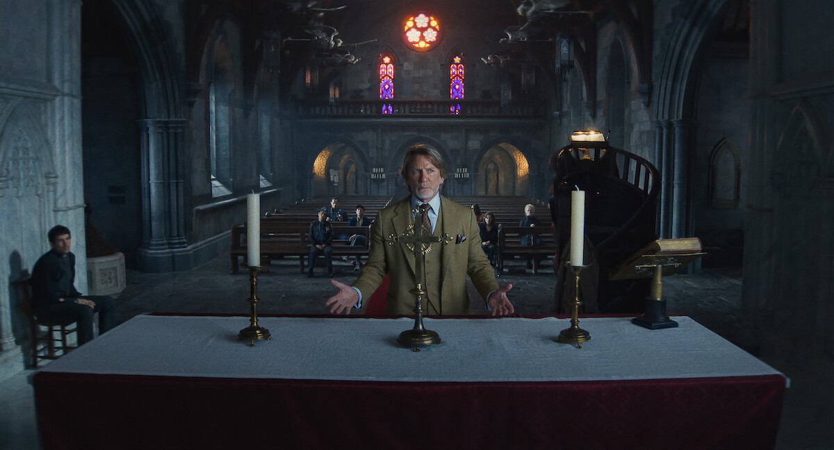 A man in a suit stands behind an altar in a dimly lit, Gothic church with stained glass windows. Several people sit in pews, creating a solemn and tense mood. The environment is grand, mysterious, and atmospheric.