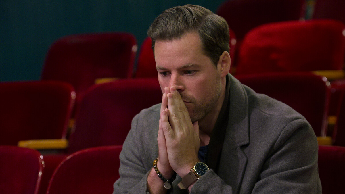 Dave sits with his hands clasped.