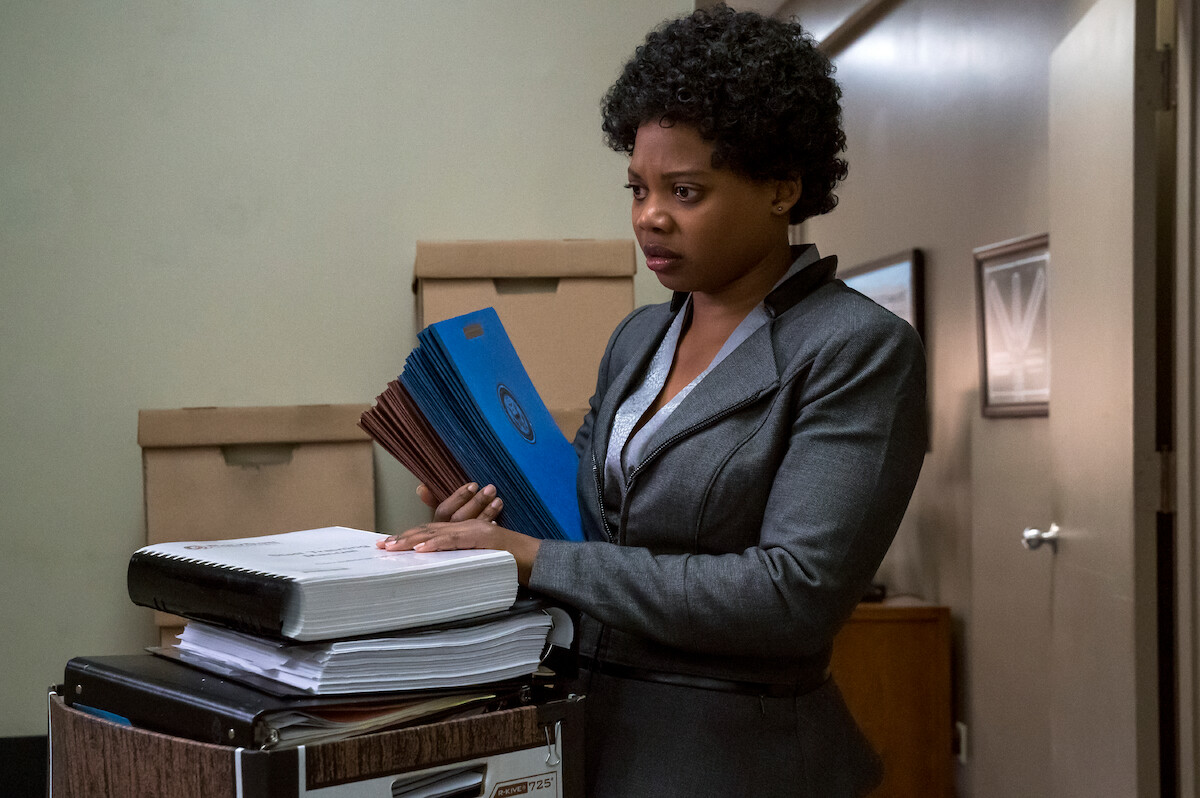Susan Heyward as Tamika Ward wears a gray business suit and holds folders in an office in Season 7 of ‘Orange Is the New Black.’ 