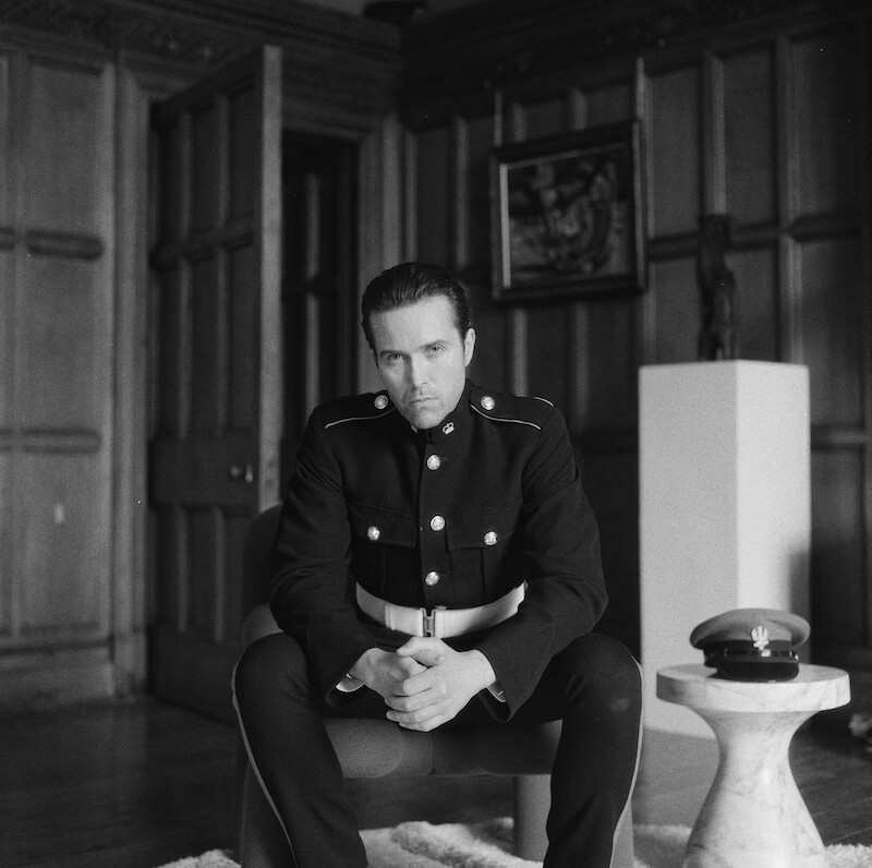 Black-and-white image of Emmett J. Scanlan as Shane Tessier wearing a uniform behind the scenes in Season 1 of 'Fool Me Once'