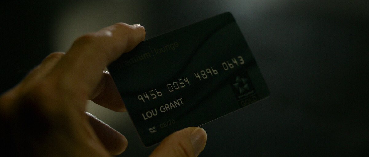 A hand holds a credit card that bears the name ‘Lou Grant.’