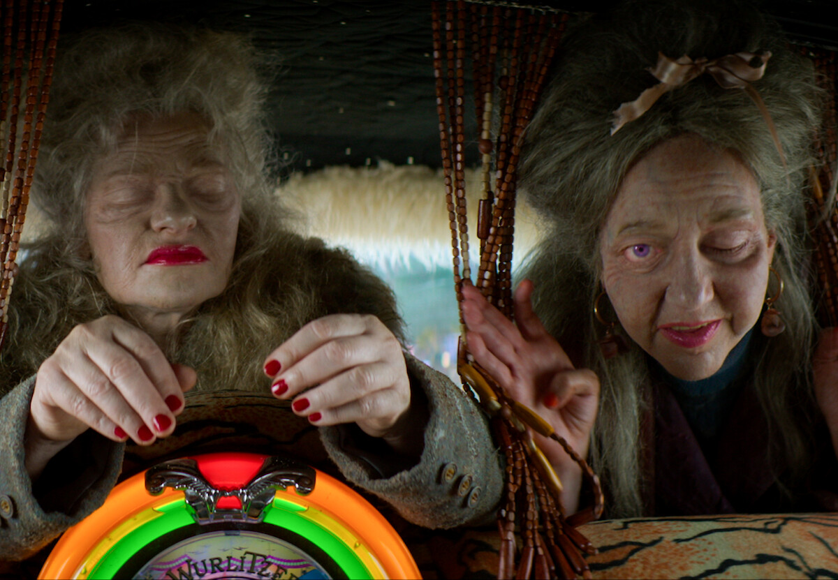 Duas personagens representando mulheres idosas e de olhos fechados olham para trás a partir dos bancos da frente de um carro