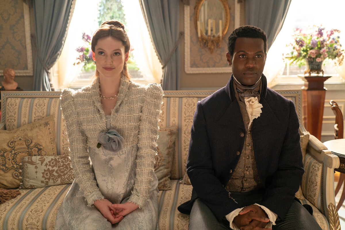 Hannah Dodd as Francesca Bridgerton and Victor Alli as John Stirling sit on a couch together in Season 3 of ‘Bridgerton.’