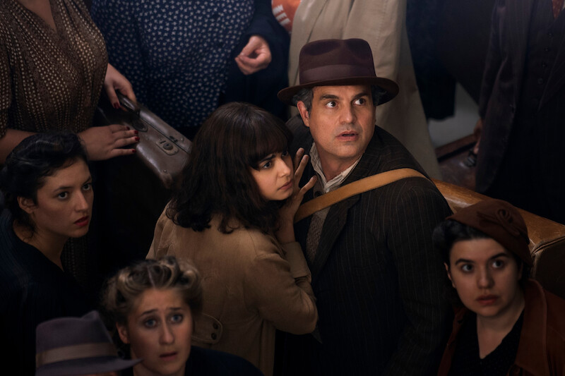 (L to R) Aria Mia Loberti as Marie-Laure, Mark Ruffalo as Daniel LeBlanc  - they are standing in a crowd, while looking up in shock at something offscreen. 