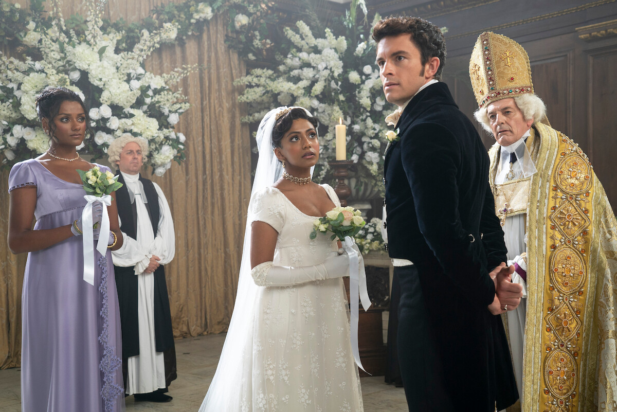 Edwina (Charithra Chandran) and Anthony (Jonathan Bailey) look stressed at the altar as maid of honor Kate (Simone Ashley) looks on.