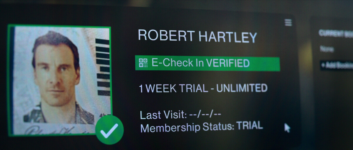 A photo of Michael Fassbender on a computer screen next to text reading “Robert Hartley E-Check-In VERIFIED.”