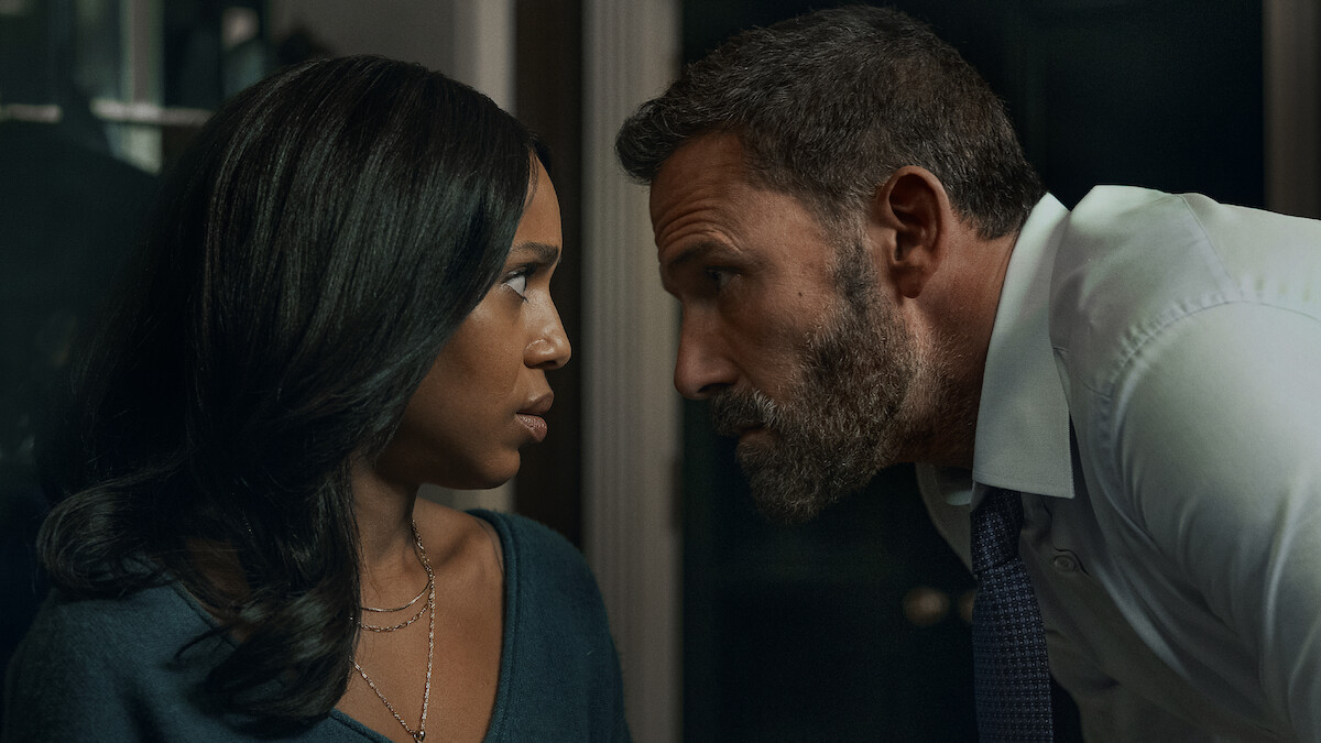 A serious man in a dress shirt and tie leans in close to a concerned woman indoors, their faces inches apart, suggesting tension or intense conversation in a dimly lit room.