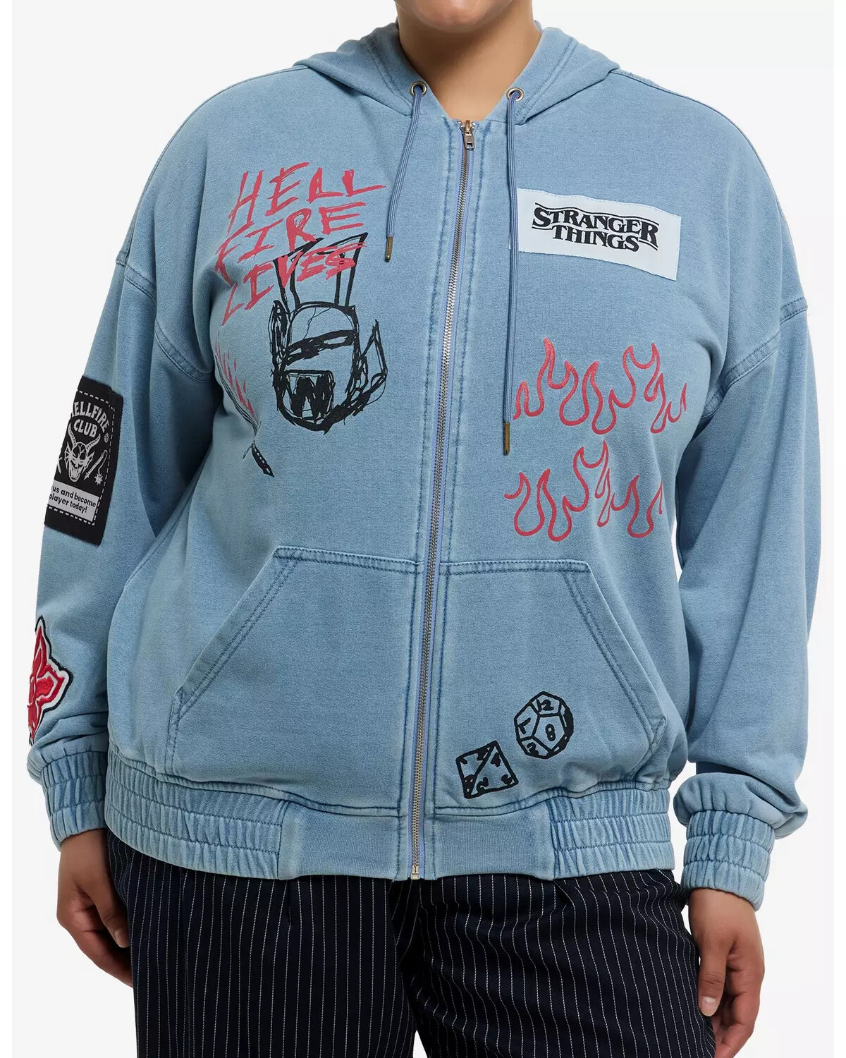 A person wearing a light blue Stranger Things-themed hoodie with various patches, red flames, and Hellfire Club graphics, standing in a well-lit indoor setting with a casual and fan-inspired vibe.
