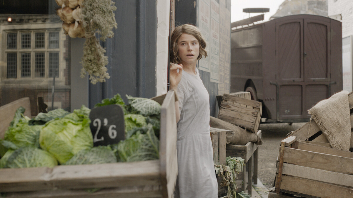 Jessie Buckley as Rose Gooding hides behind a partition at a produce market in ‘Wicked Little Letters.’