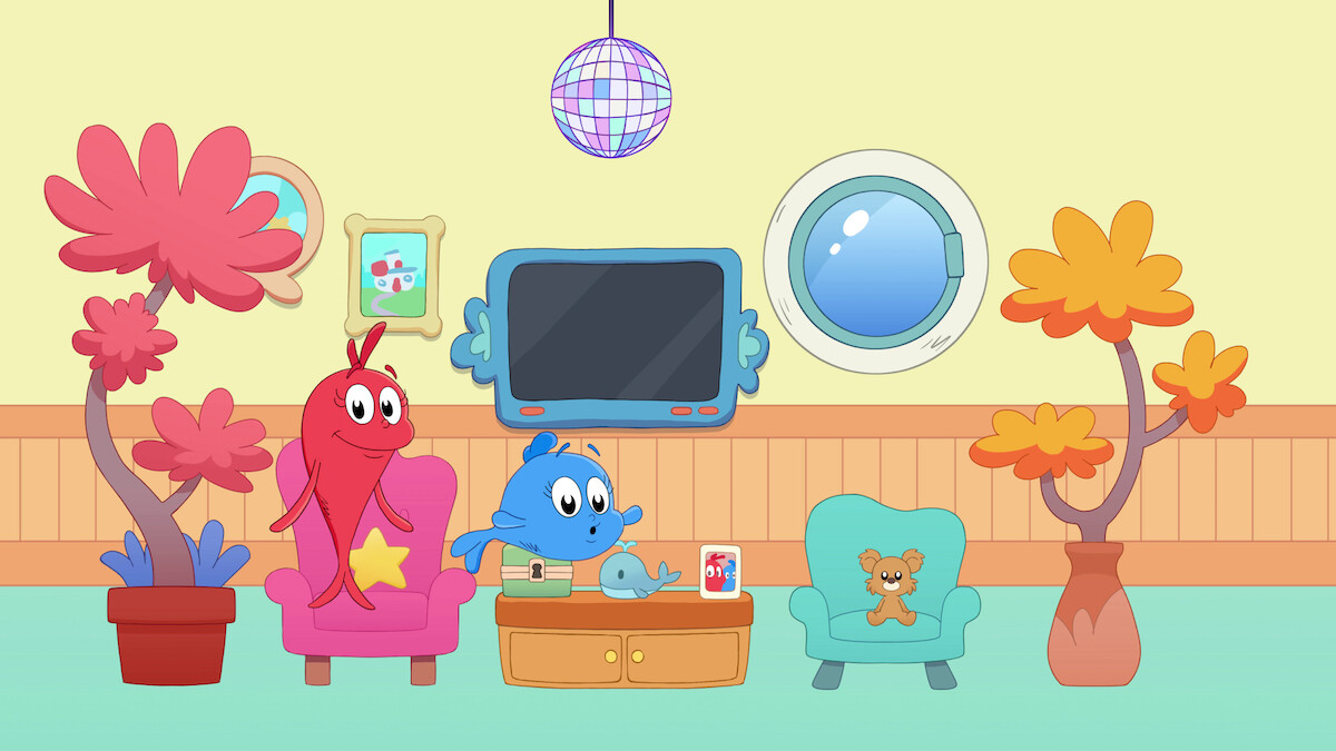 Two colorful cartoon characters sit in a cozy living room with armchairs, potted plants, a wall-mounted TV, a circular window, a disco ball, a coffee table with a toy, and a teddy bear in a blue chair.