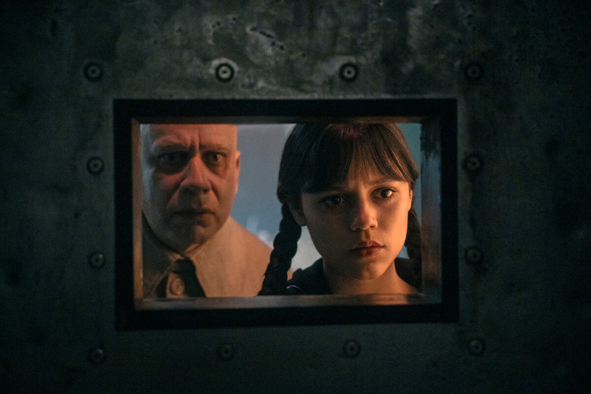 Fred Armisen as Uncle Fester and Jenna Ortega as Wednesday Addams look through a wicket in Willow Hill in ‘Wednesday’ Season 2.