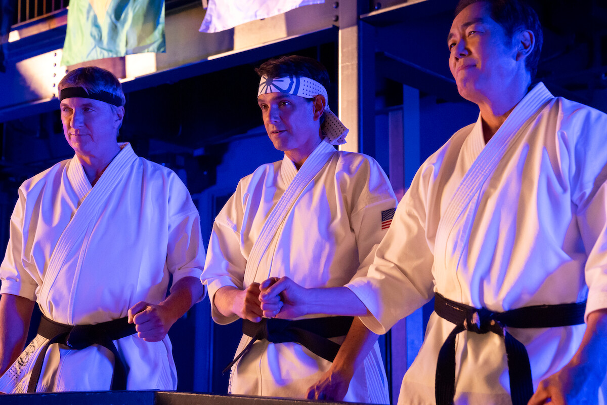 William Zabka as Johnny Lawrence, Ralph Macchio as Daniel LaRusso, and Yuji Okumoto as Chozen bump fists in their karate uniforms in Season 6 of ‘Cobra Kai.’