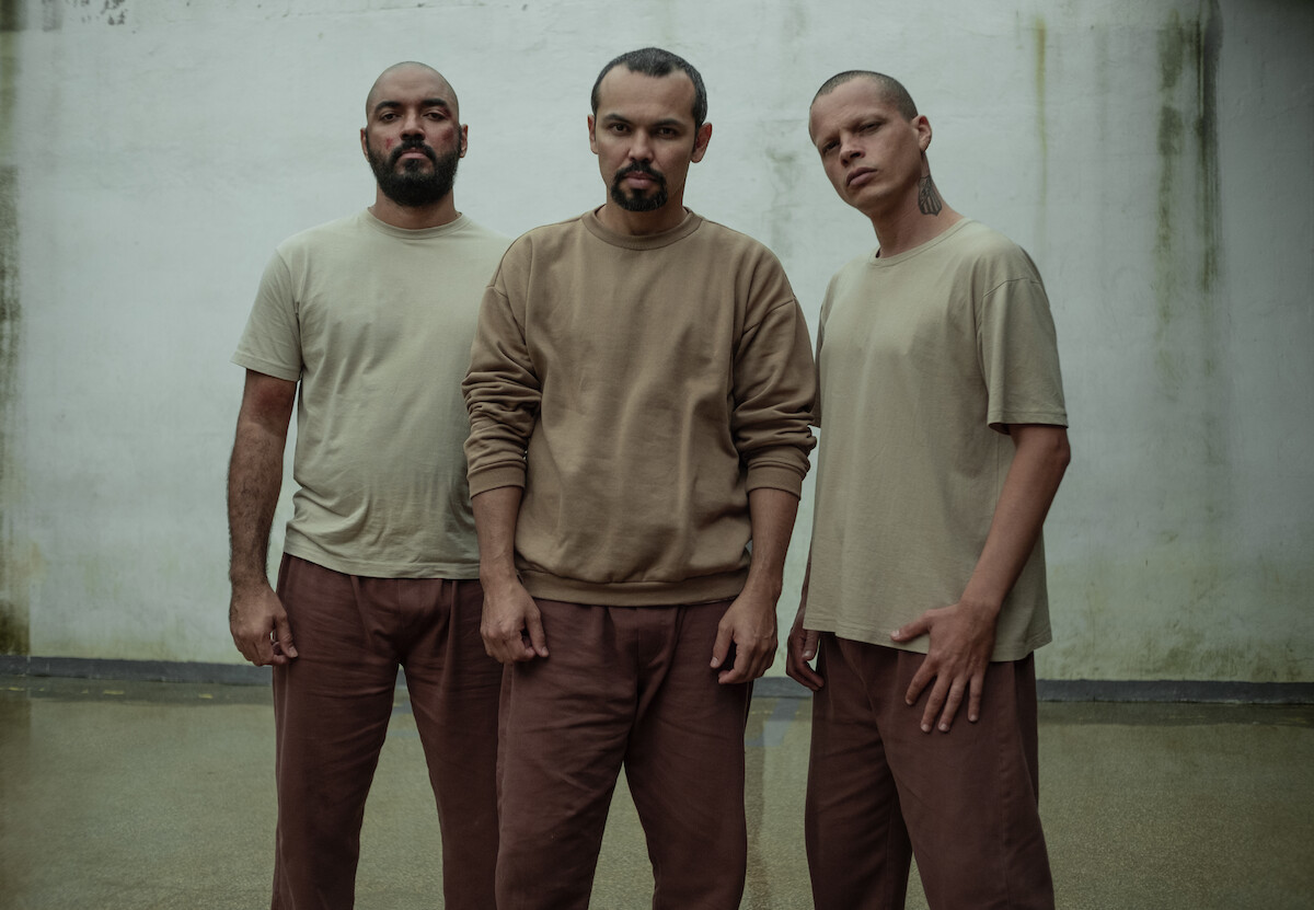 Três homens posam lado a lado em uma penitenciária