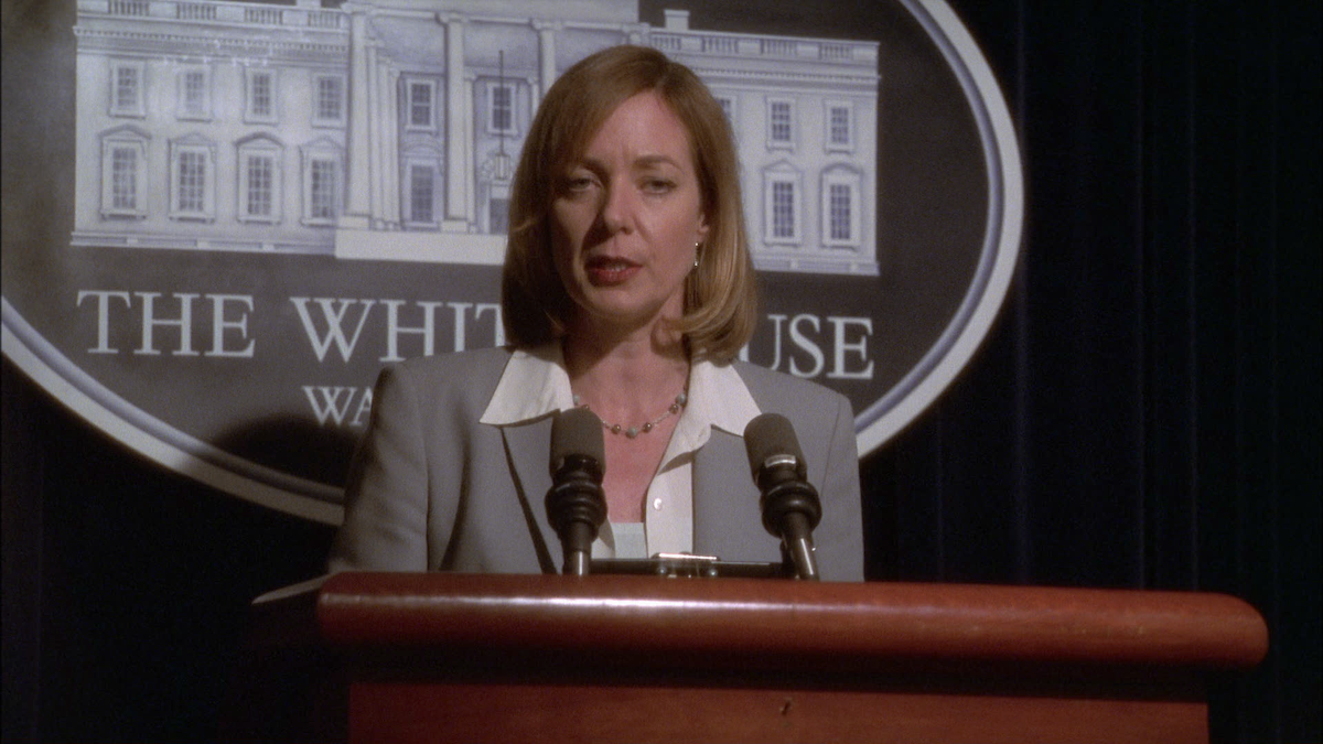 A woman stands at a podium with microphones, delivering a speech in front of a White House backdrop, suggesting a press conference or official announcement in a formal setting.
