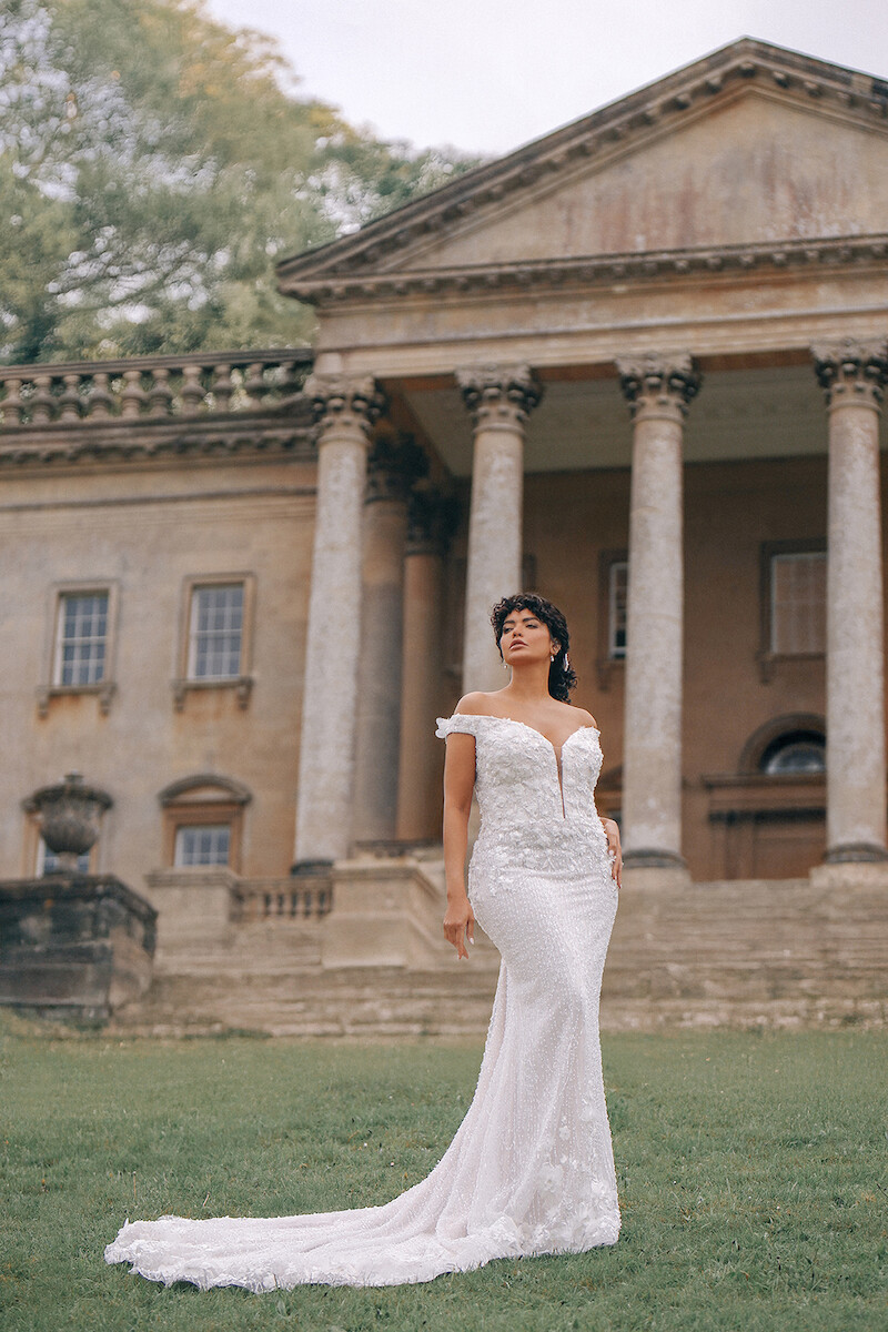 Woman in bridal dress poses with ornate building behind her.