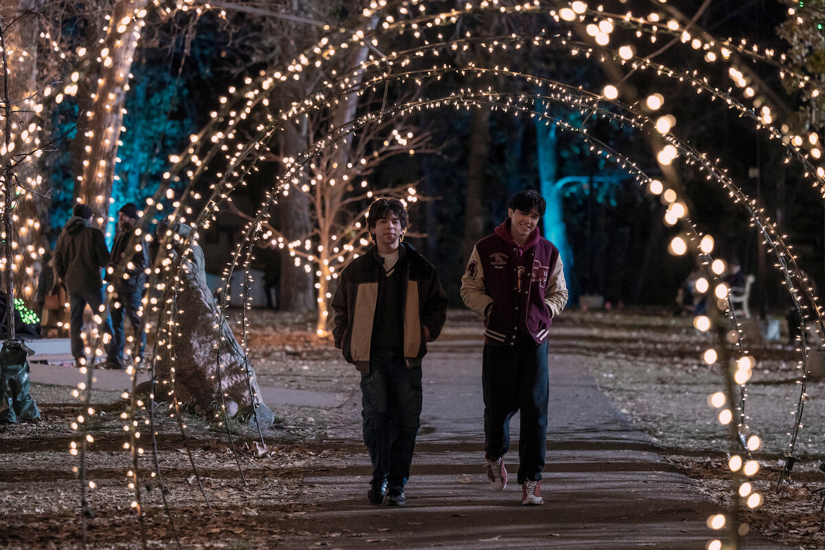 Myles Perez as Lee and Isaac Arellanes as Isaac walk through an archway of lights in a park in ‘My Life with the Walter Boys’ Season 2.