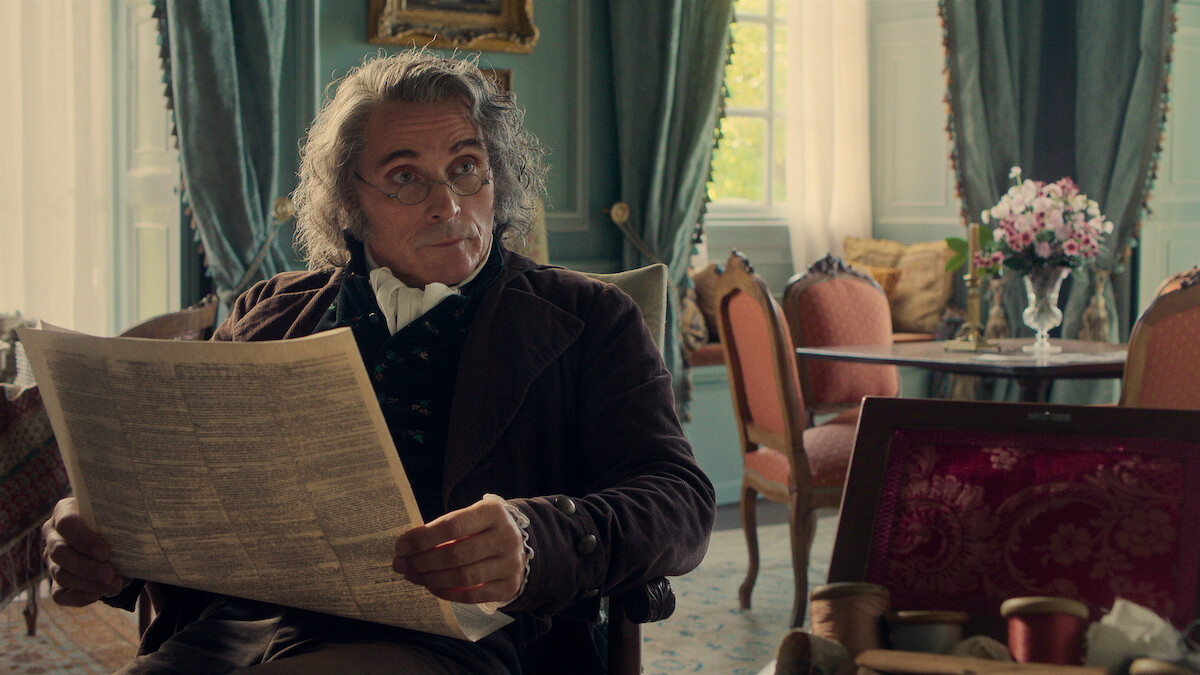 Older man in period clothing sits in ornate room with elegant chairs, green curtains, and a vase of flowers, reading a newspaper and gazing thoughtfully to the side.