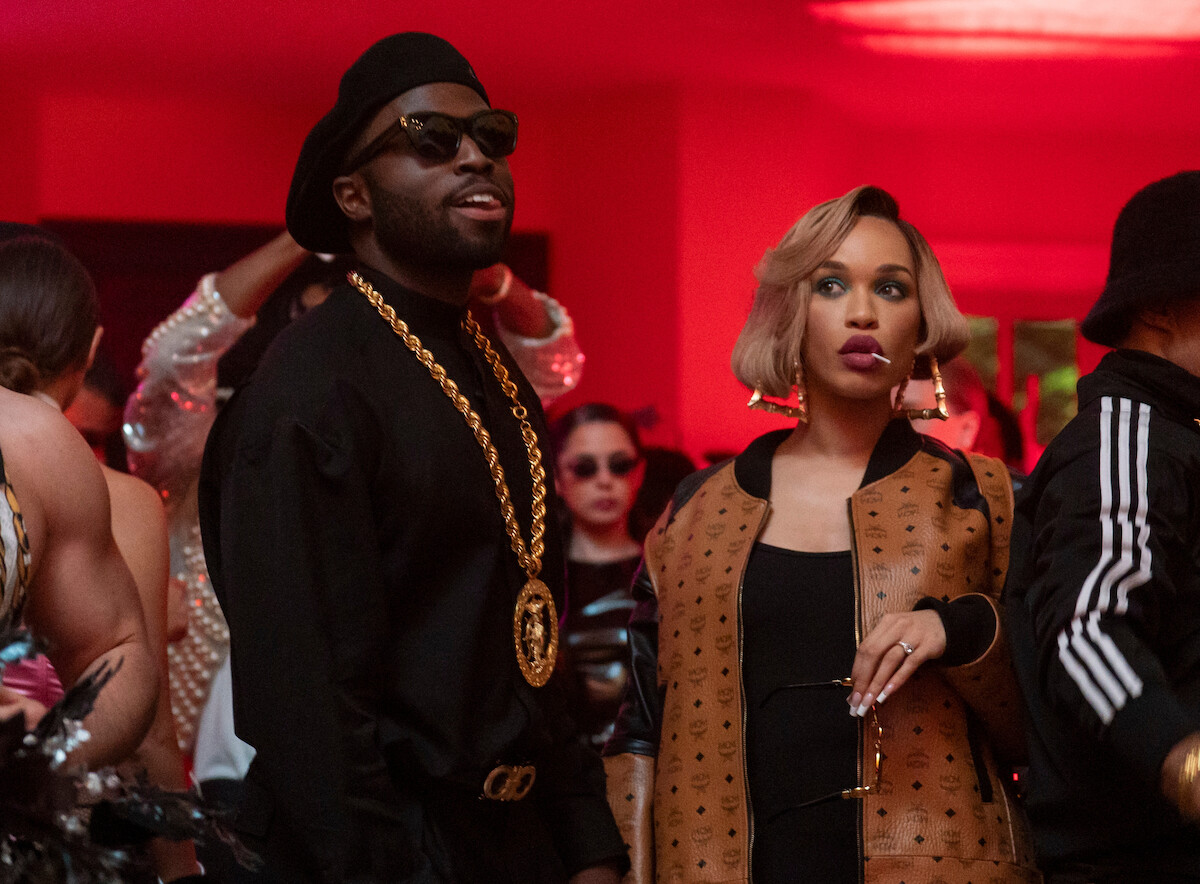 Man and woman dressed stylishly at a party with red lighting, surrounded by other people in fashionable clothes, festive atmosphere, accessories, and sunglasses.