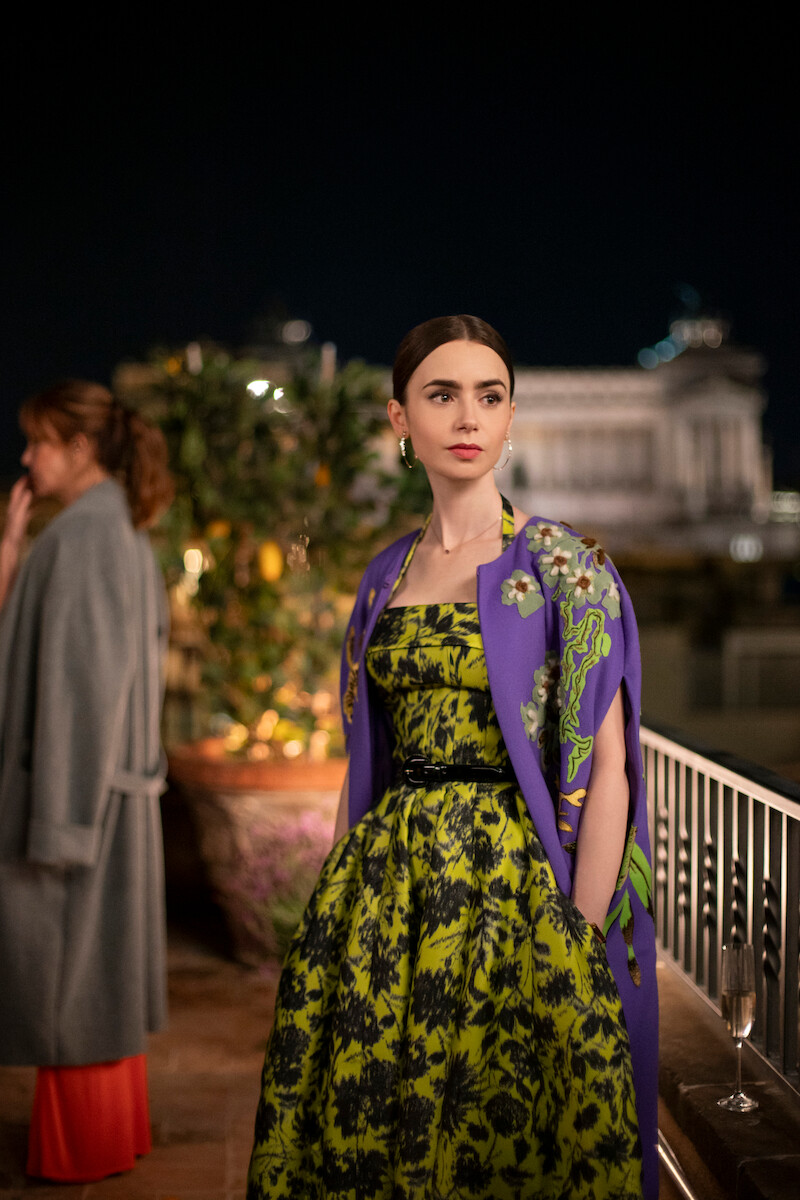 Lily Collins as Emily stands outside at night by a river in Season 4 of 'Emily in Paris'