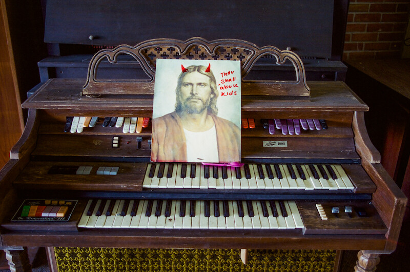 An old piano with a portrait of Jesus that reads "Thou shall abuse kids."