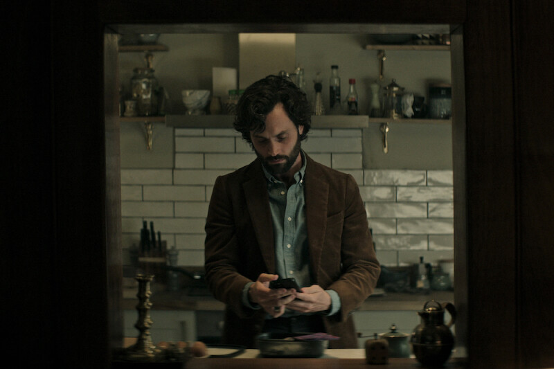 Badgley as Joe Goldberg looking at his phone