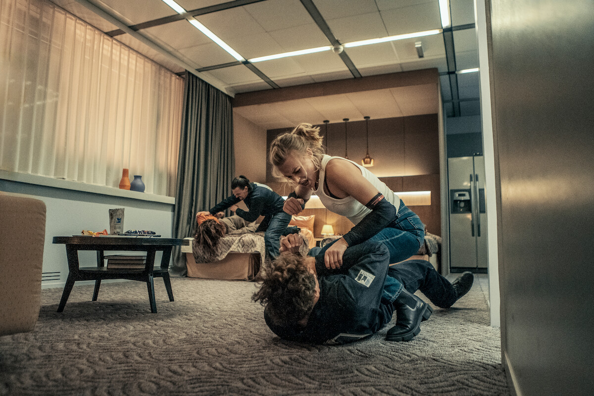 Jeanne Goursaud as Sara Wulf holds down a man on a carpeted apartment room floor in an image from the film ‘Exterritorial.’