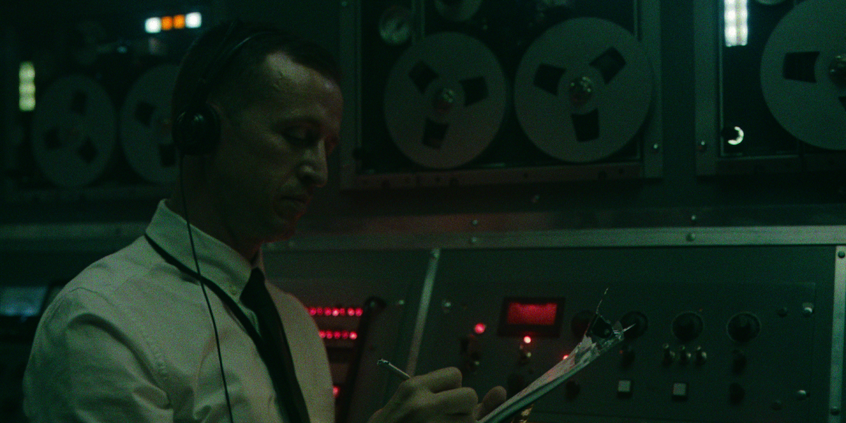 A man wearing headphones writes on his clipboard.