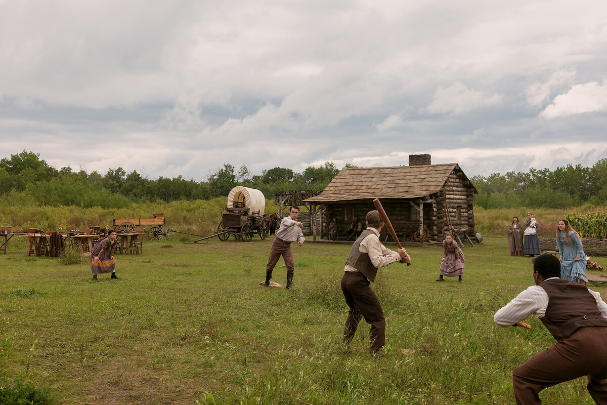 A group of people play baseball in front of a cabin.