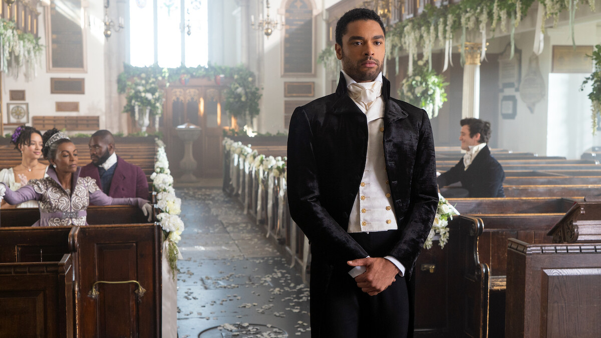 A man in formal 19th-century attire stands in the aisle of an ornately decorated church with flowers and pews, while guests sit in the background, suggesting a wedding or important ceremony.