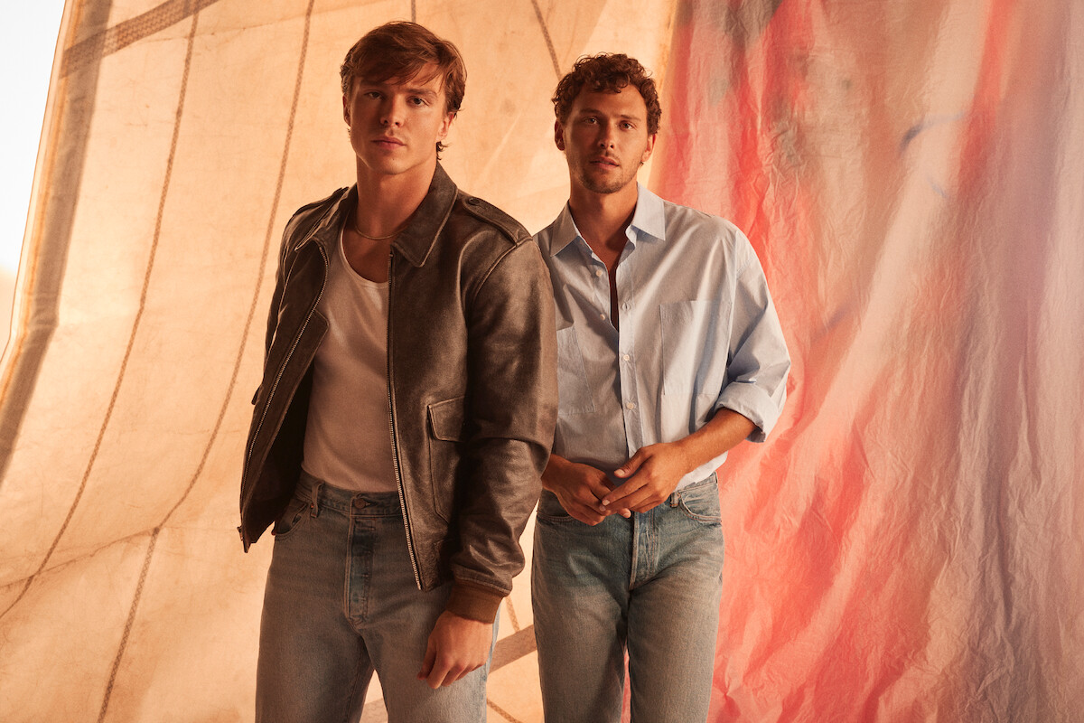From left, Nicholas Alexander Chavez and Cooper Koch looking directly to camera in front of a sail.