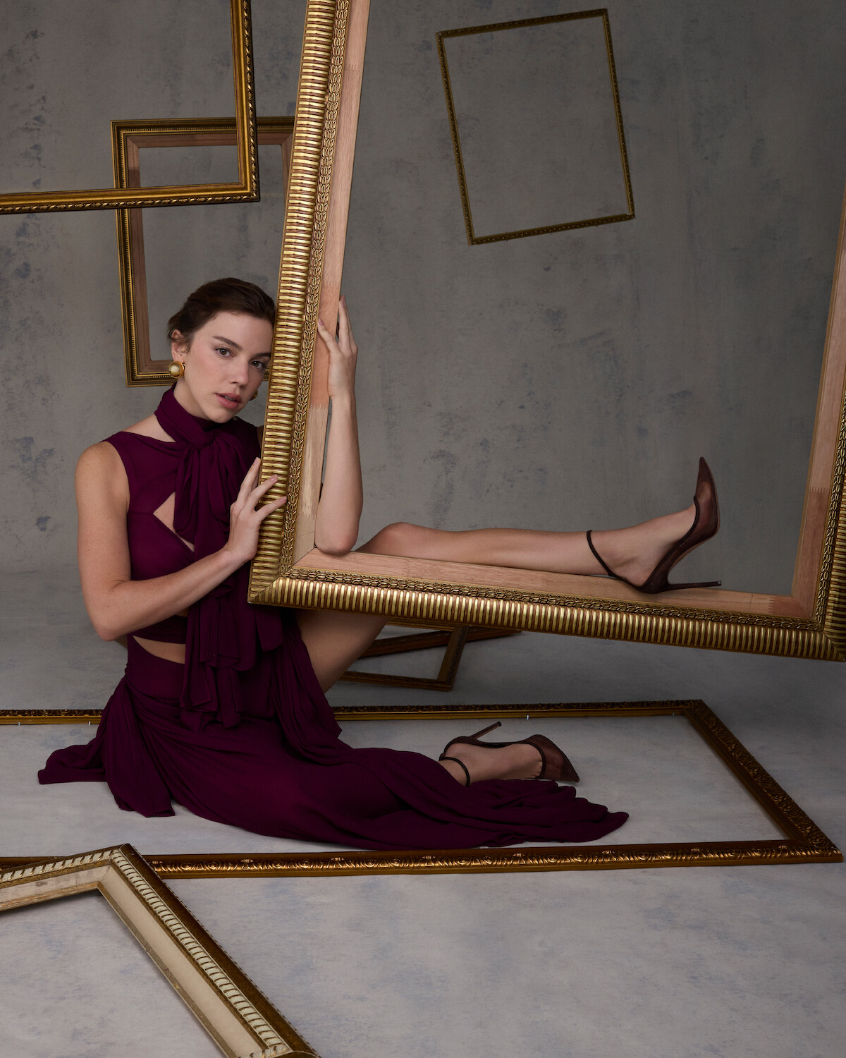 A atriz Alice Wegmann, uma mulher jovem, de cabelos castanhos e presos usa vestido vinho enquanto segura uma grande moldura dourada