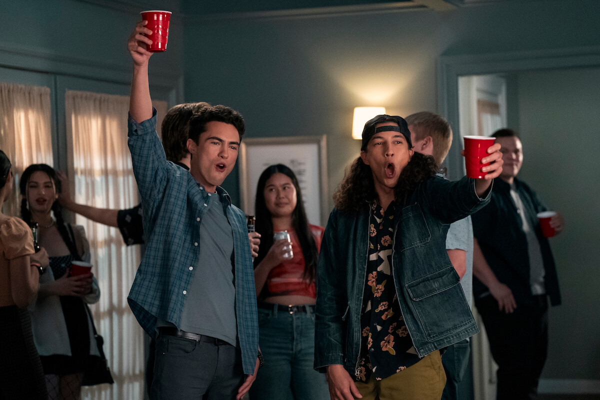 Darren Barnet as Paxton Hall-Yoshida and Benjamin Norris as Trent in Never Have I Ever Season 3 hold up red plastic cups at a party. 