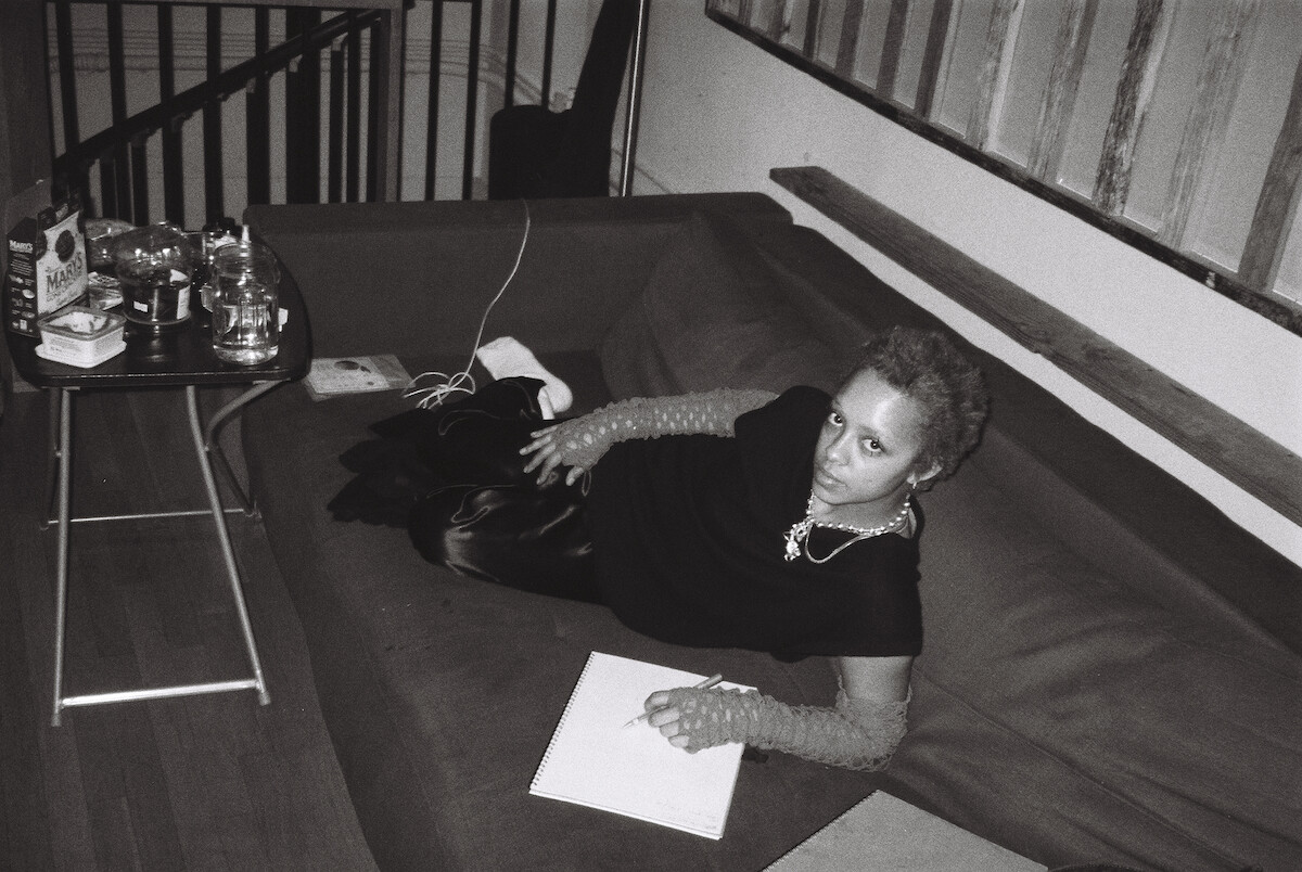 Kelsey Lu lounges on a couch writing on a white pad.
