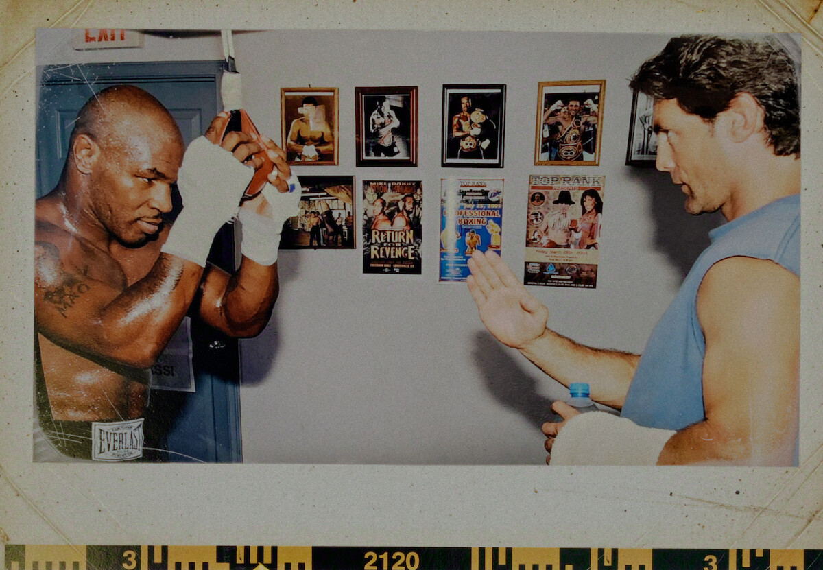 O lutador Myke Tyson, um homem negro e de tabelos raspados, treina boxe com um auxiliar