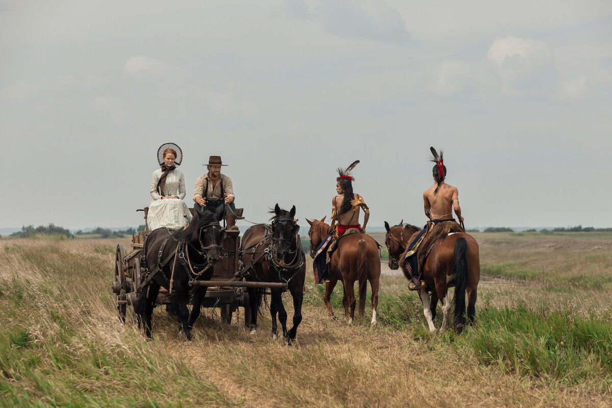 Pessoas em uma carroça cruzam com pessoas a cavalo.