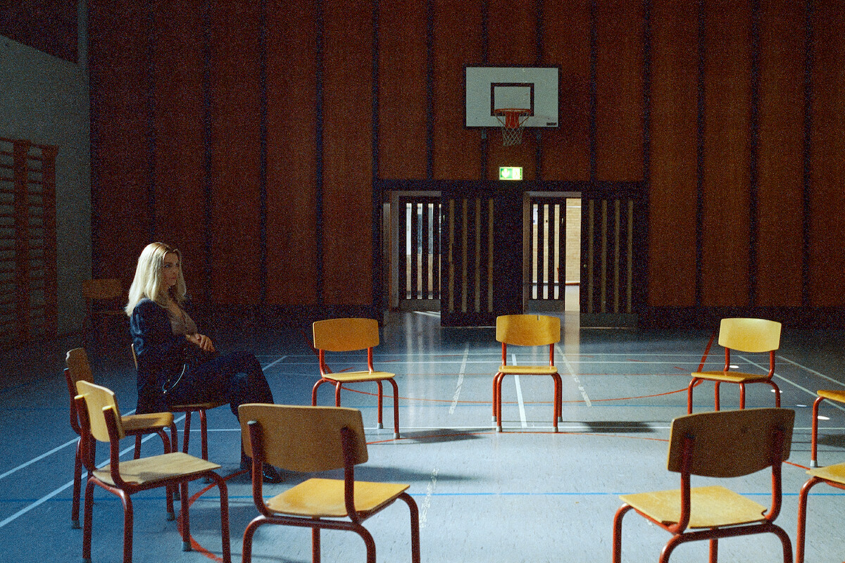 Marie Bach Hansen as Cecilie sits in a gymnasium among a circle of empty chairs in an image from the series ‘Secrets We Keep.’