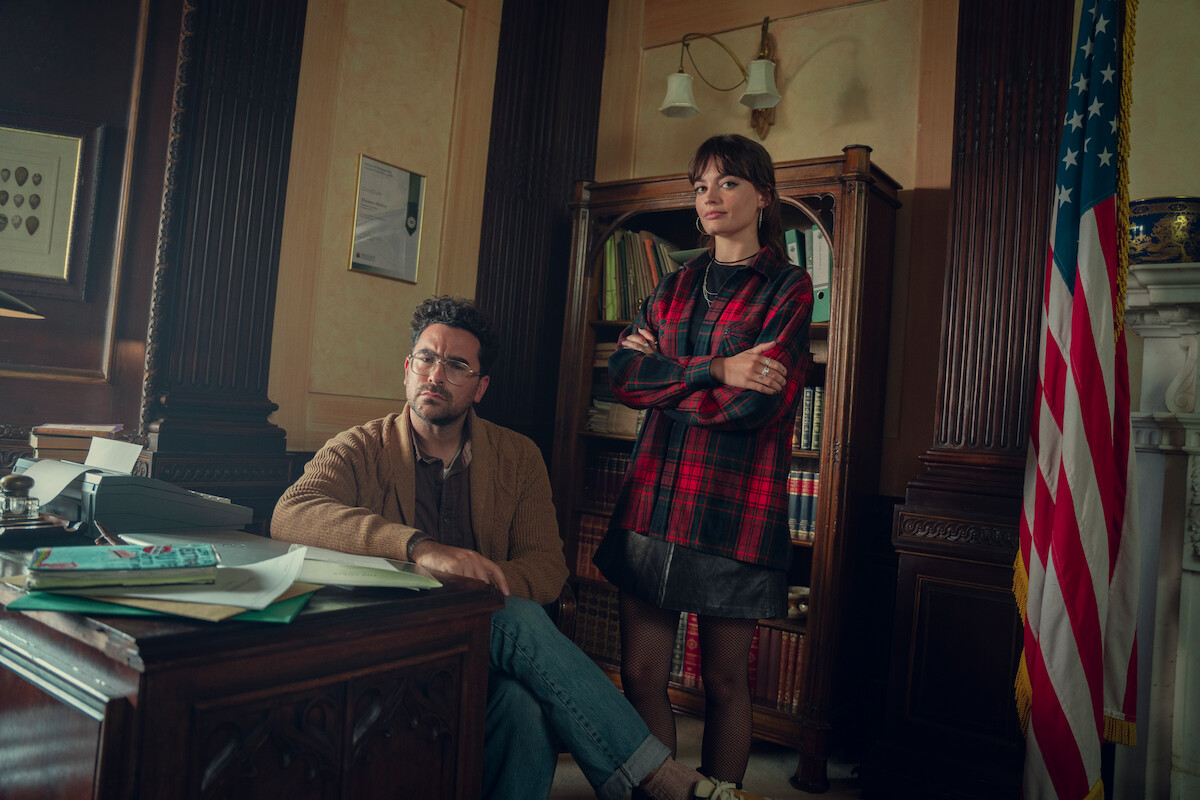 Dan Levy as Thomas Molloy and Emma Mackey as Maeve pose together in an office at school in Season 4 of ‘Sex Education’